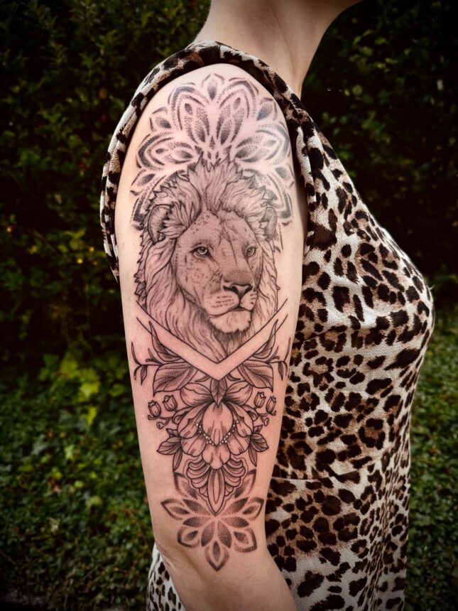 Løvetatovering med blomster på overarm